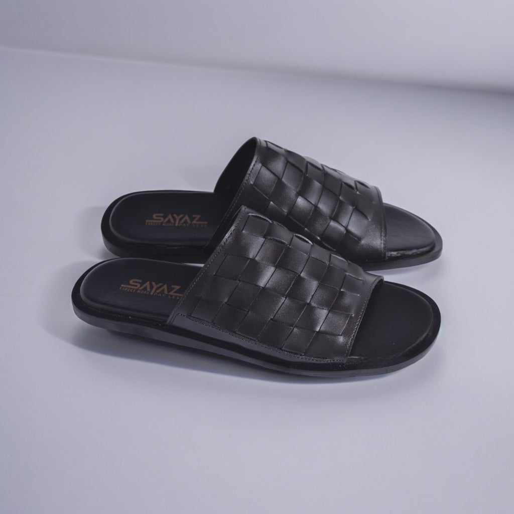 A pair of black leather slippers with a textured pattern, displayed against a white background.