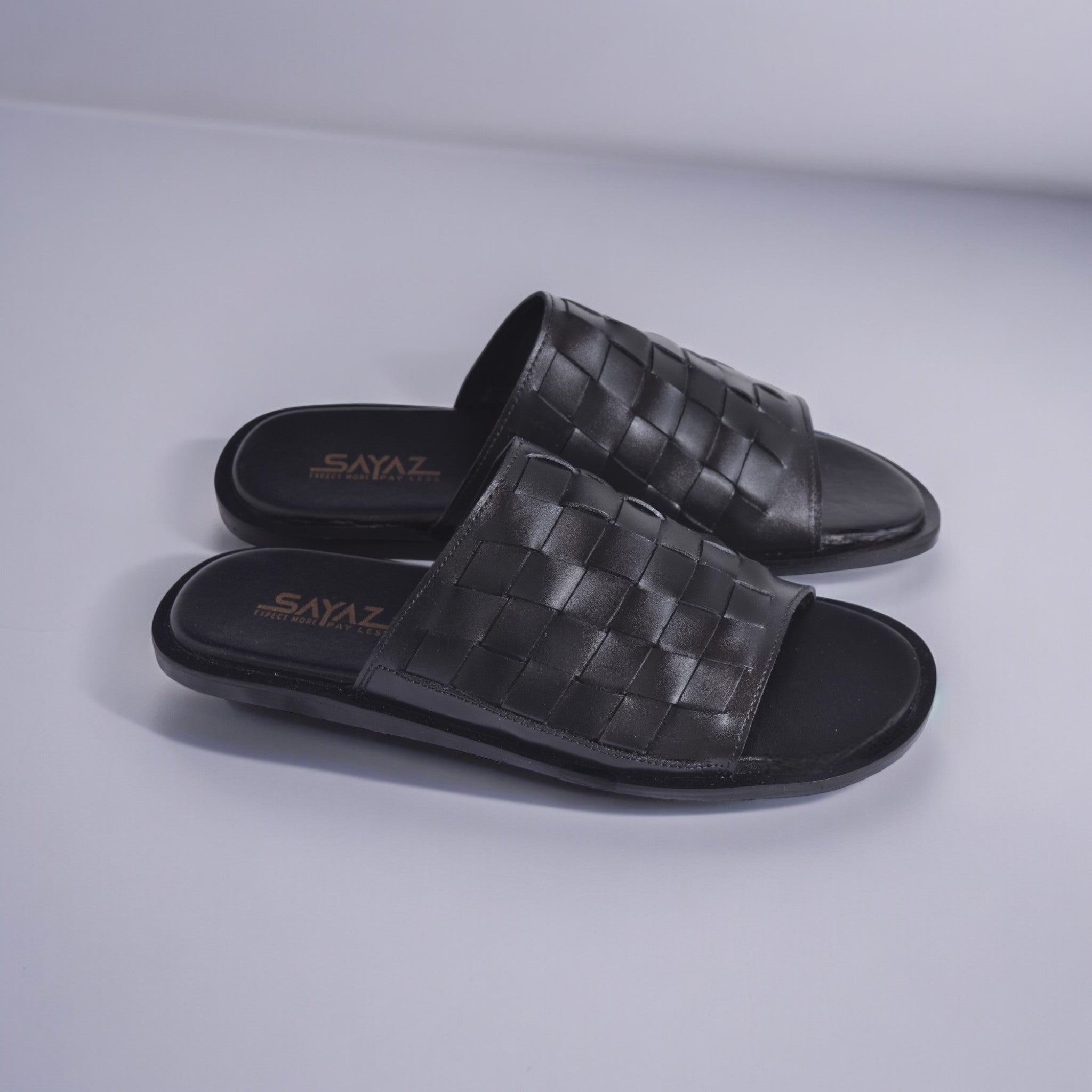A pair of black leather slippers with a textured pattern, displayed against a white background.