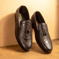 A pair of black leather casual shoes with a lace-up closure and a decorative metal emblem on the top.