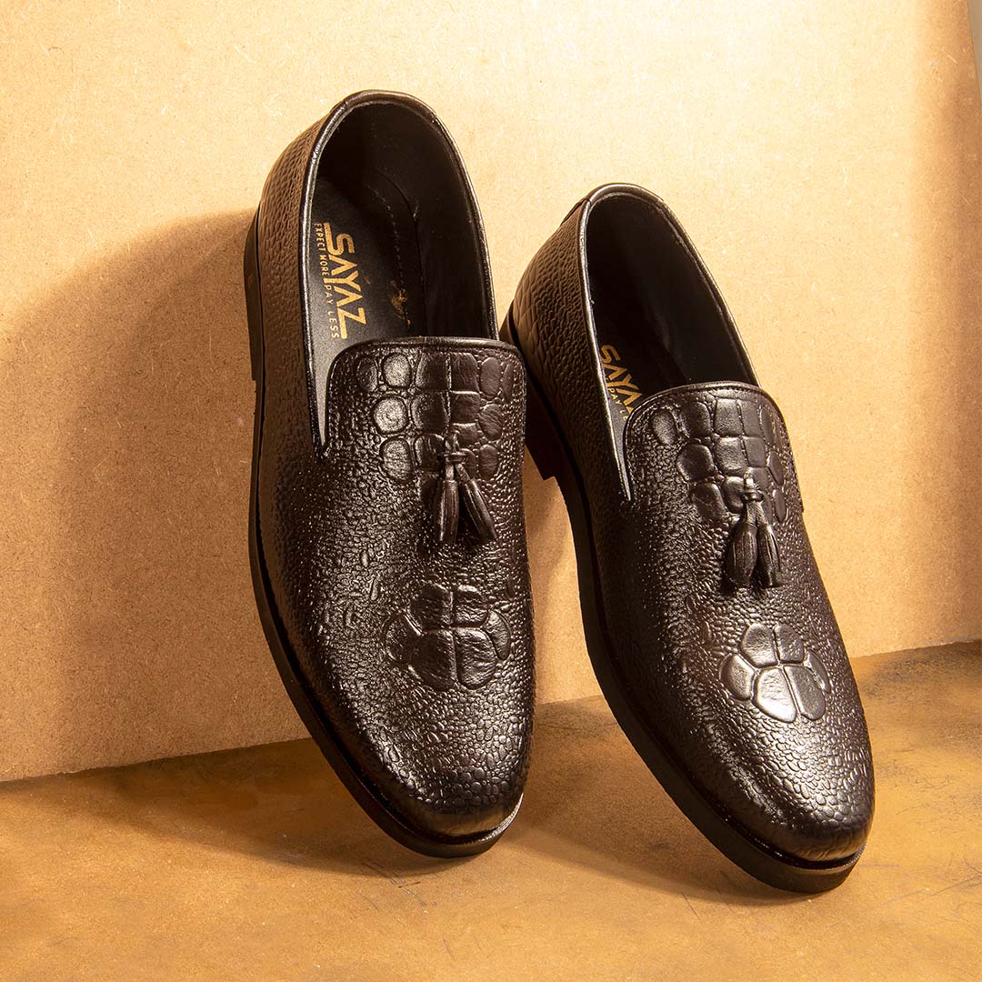 A pair of black leather casual shoes with a lace-up closure and a decorative metal emblem on the top.